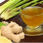A steaming cup of ginger and lemongrass tea placed next to fresh ginger rhizomes and green lemongrass stalks on a wooden surface